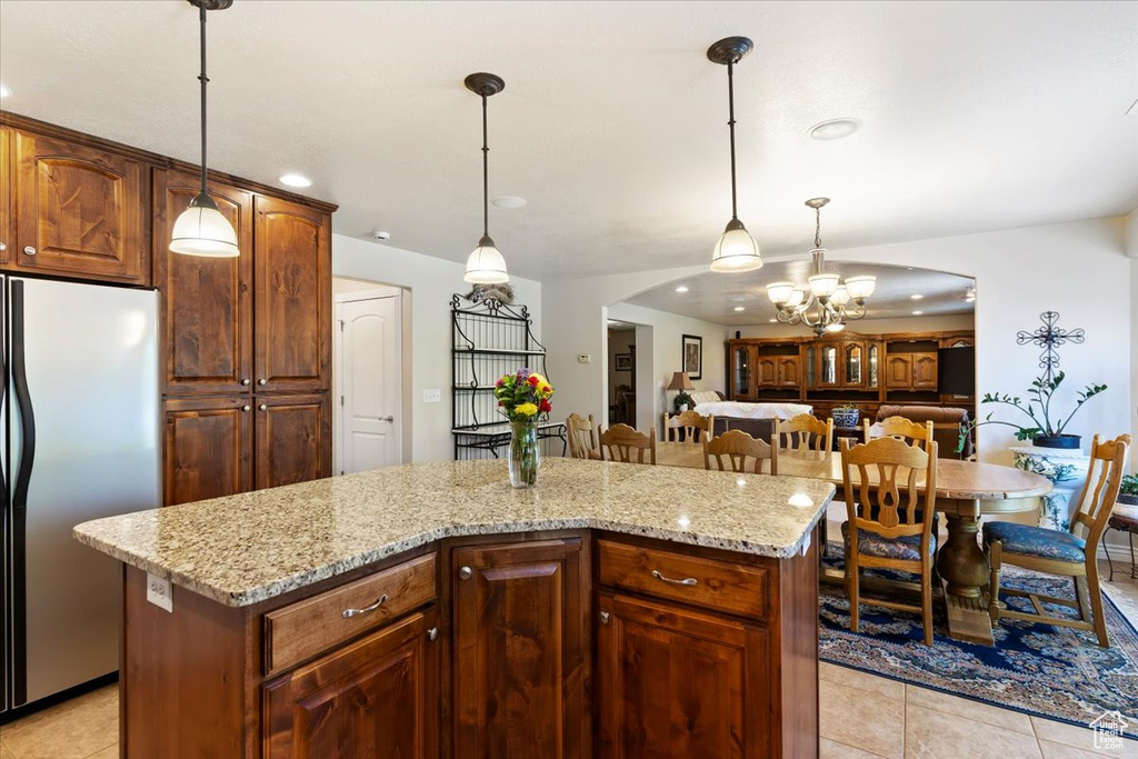 Kitchen featuring stainless steel refrigerator, a chandelier, light tile patterned flooring, a kitchen island, and light stone counters