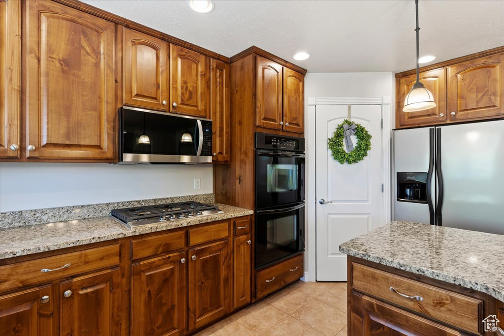 Kitchen with stainless steel appliances, light stone countertops, decorative light fixtures, light tile patterned floors, and brown cabinetry