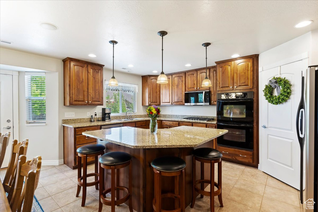 Kitchen featuring stainless steel appliances, a sink, light tile patterned flooring, light stone countertops, and a kitchen breakfast bar
