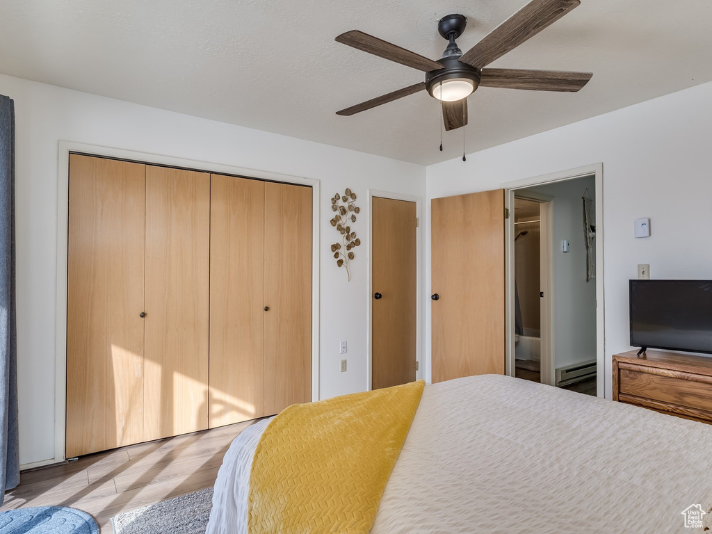 Bedroom with a baseboard radiator, light wood-style flooring, and a ceiling fan