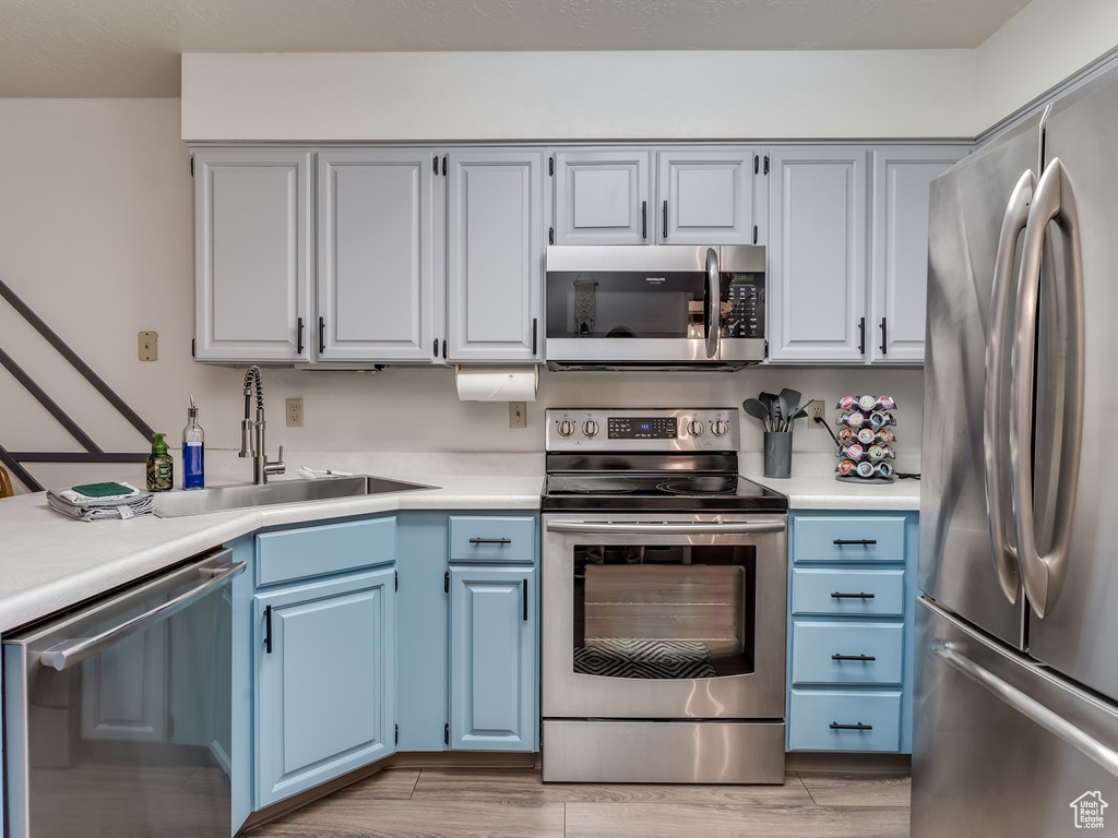 Kitchen with appliances with stainless steel finishes, blue cabinets, light countertops, and a sink