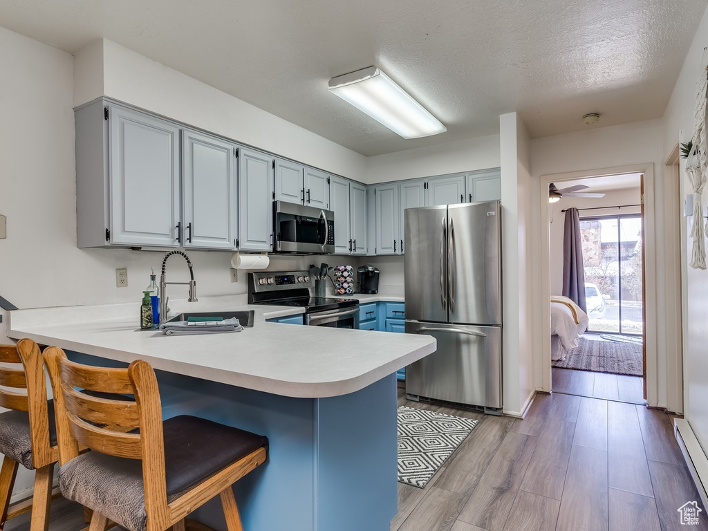Kitchen featuring appliances with stainless steel finishes, a peninsula, light countertops, a breakfast bar area, and blue cabinets