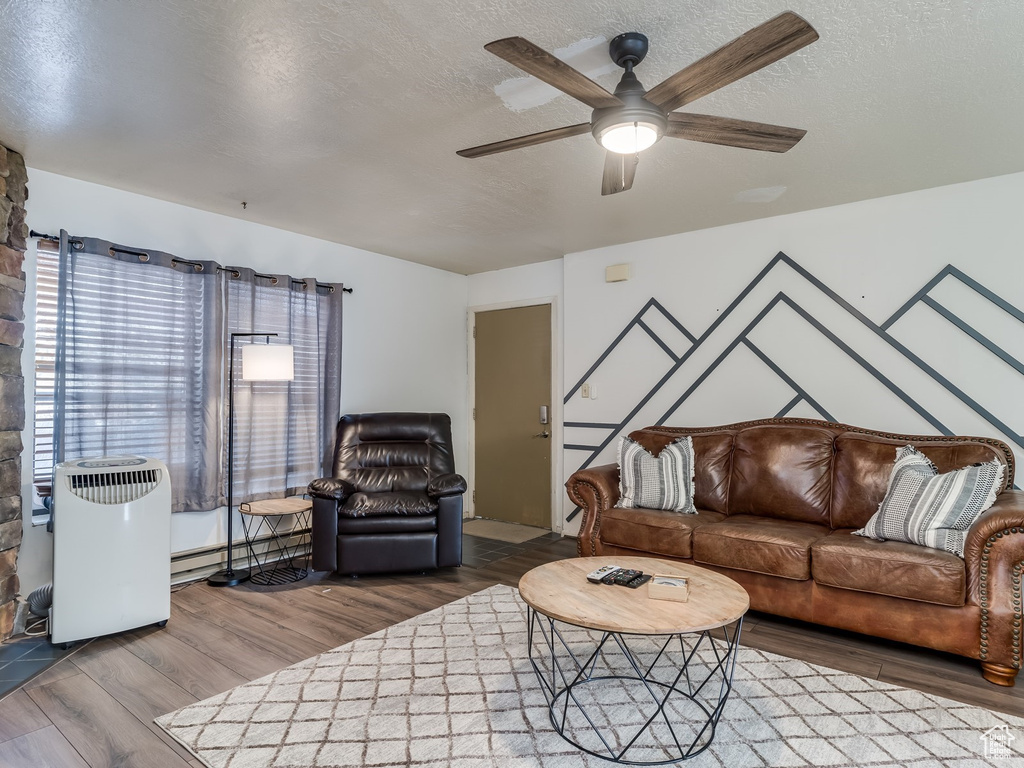 Living area featuring wood finished floors, a textured ceiling, a ceiling fan, and a baseboard heating unit