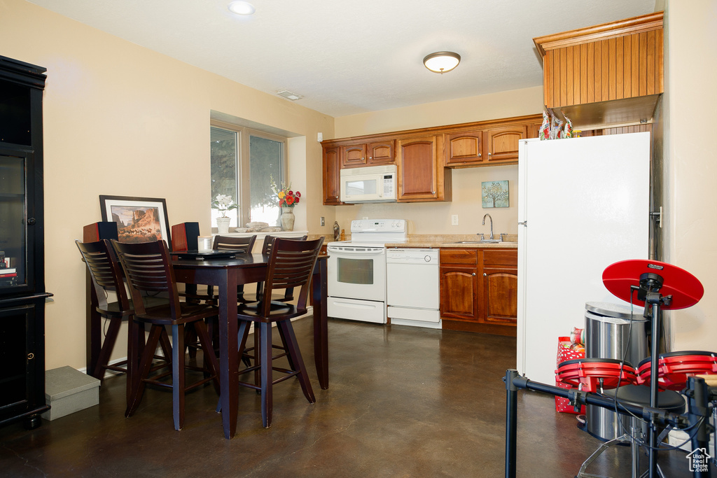 Kitchen featuring white appliances, a sink, concrete floors, brown cabinets, and light countertops