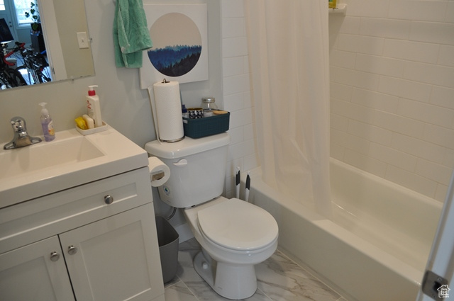 Full bath with marble look tiles, vanity, toilet, and shower / tub combo with curtain