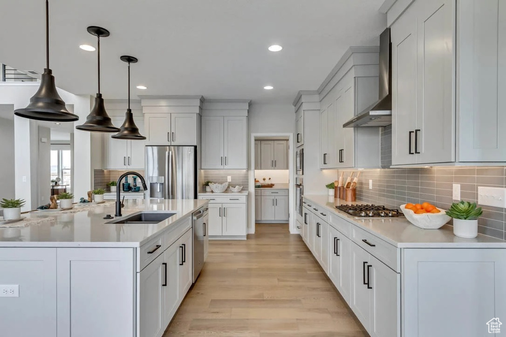 Kitchen with appliances with stainless steel finishes, wall chimney range hood, a sink, light countertops, and decorative backsplash