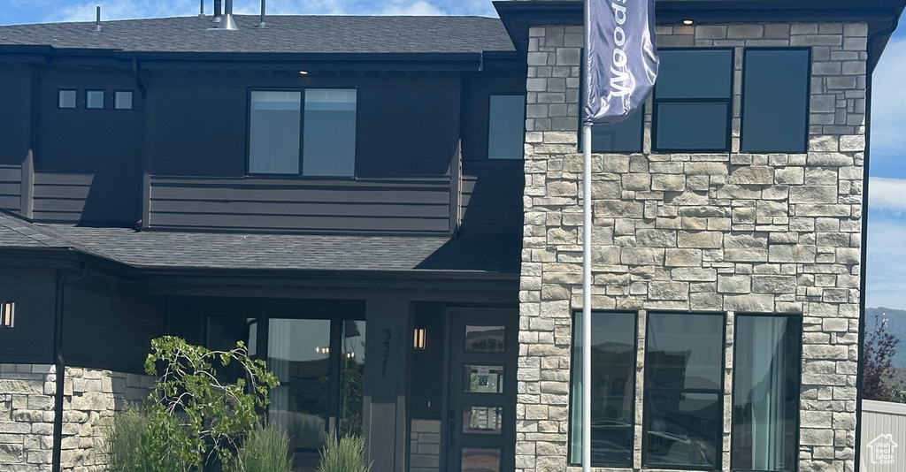 Entrance to property featuring stone siding and roof with shingles