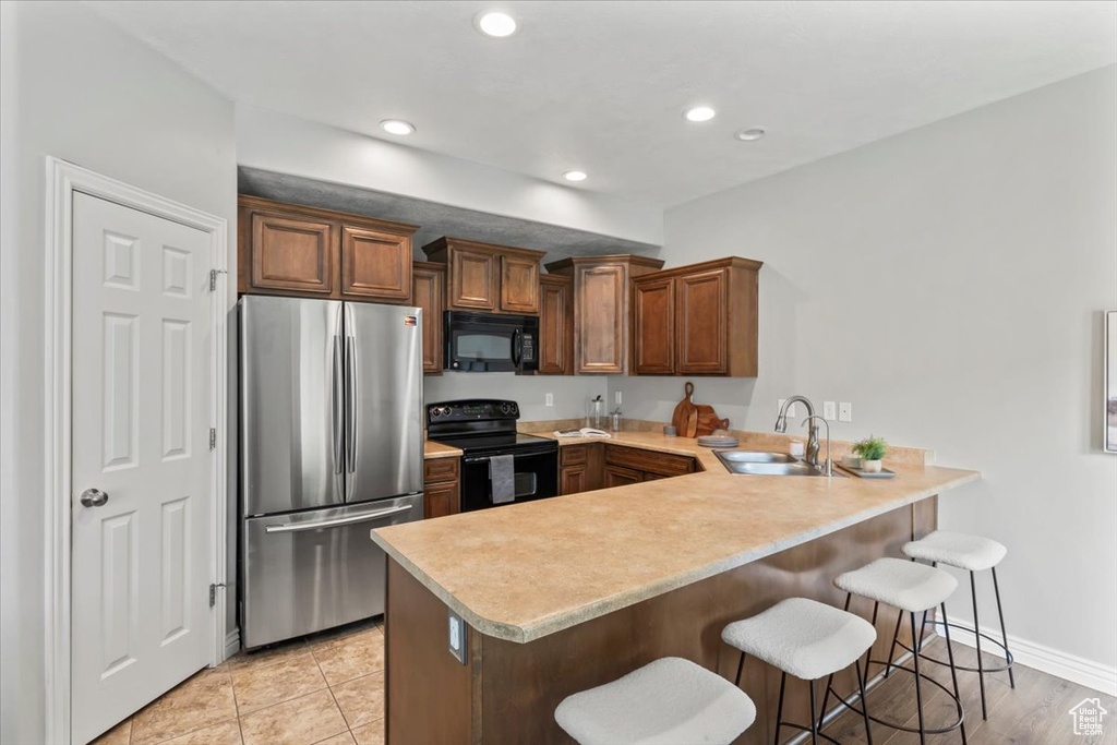 Kitchen with black appliances, a sink, a peninsula, a kitchen breakfast bar, and recessed lighting