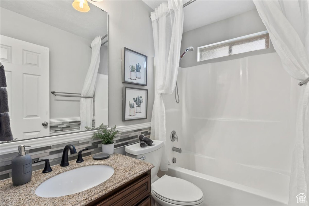 Full bath featuring shower / bath combo with shower curtain, toilet, vanity, and backsplash