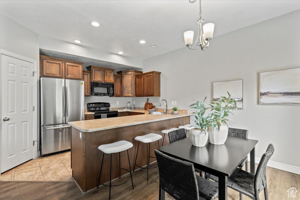 Kitchen with black appliances, a peninsula, a sink, light countertops, and a chandelier