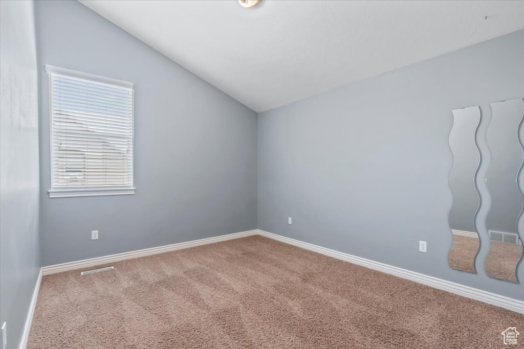 Spare room featuring vaulted ceiling, carpet, and baseboards