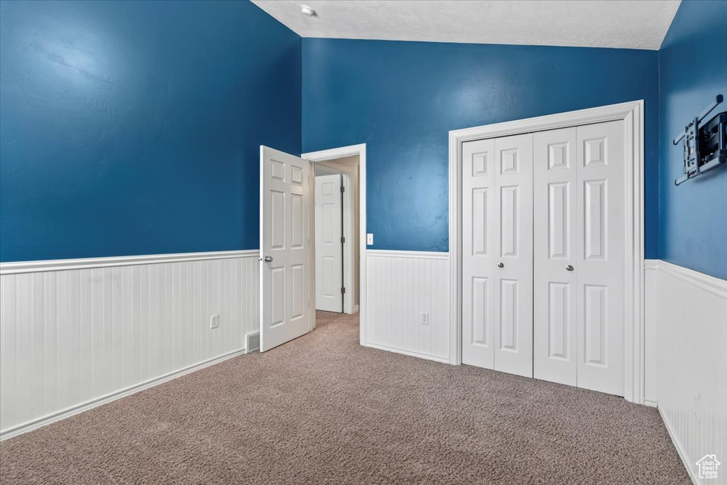 Unfurnished bedroom with a wainscoted wall, carpet, vaulted ceiling, a closet, and a textured ceiling