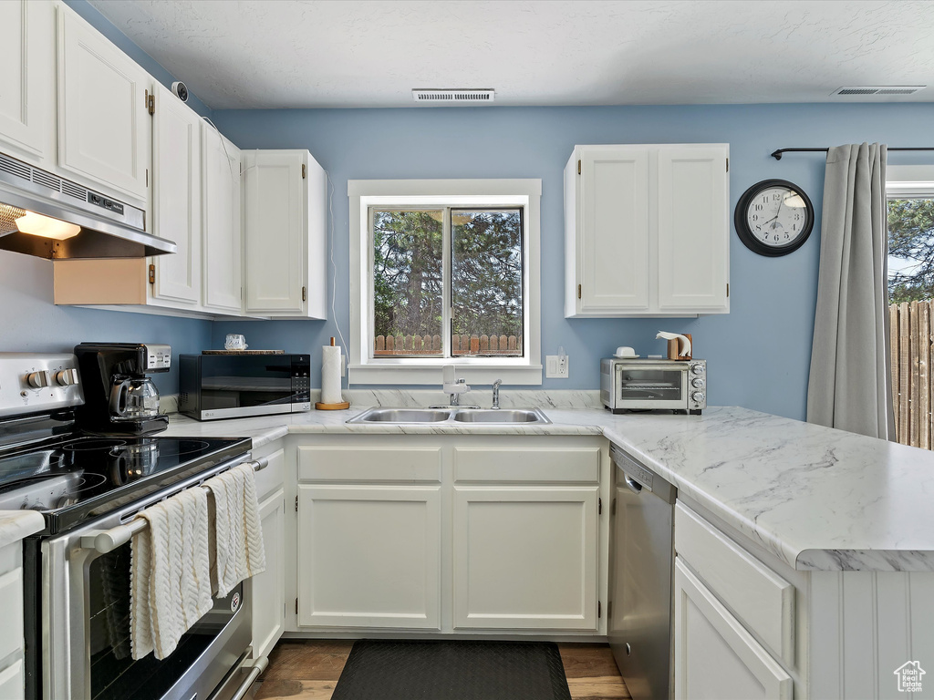 Kitchen with appliances with stainless steel finishes, a sink, under cabinet range hood, white cabinets, and a peninsula