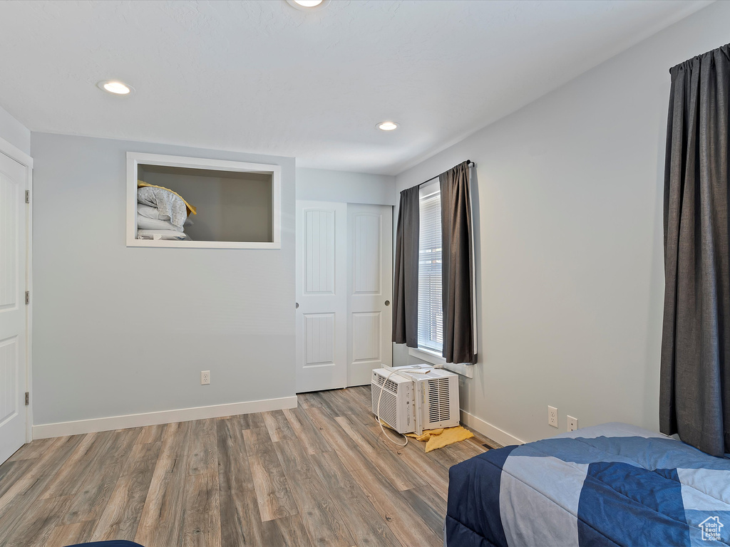 Bedroom featuring wood finished floors, recessed lighting, baseboards, and a wall mounted AC