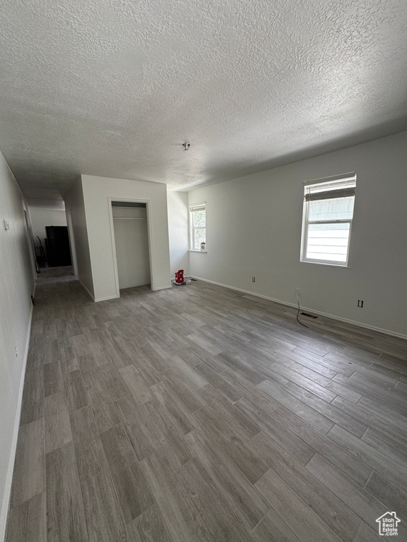 Spare room featuring healthy amount of natural light, wood finished floors, a textured ceiling, and baseboards