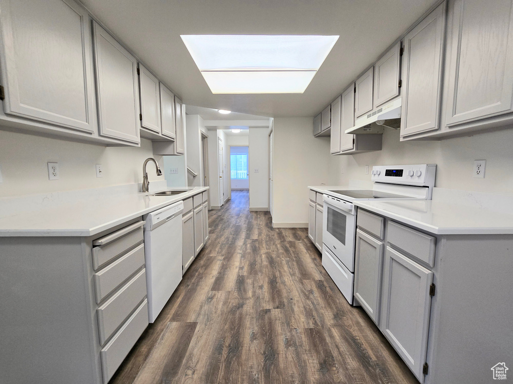 Kitchen with white appliances, gray cabinetry, under cabinet range hood, a sink, and dark wood-type flooring