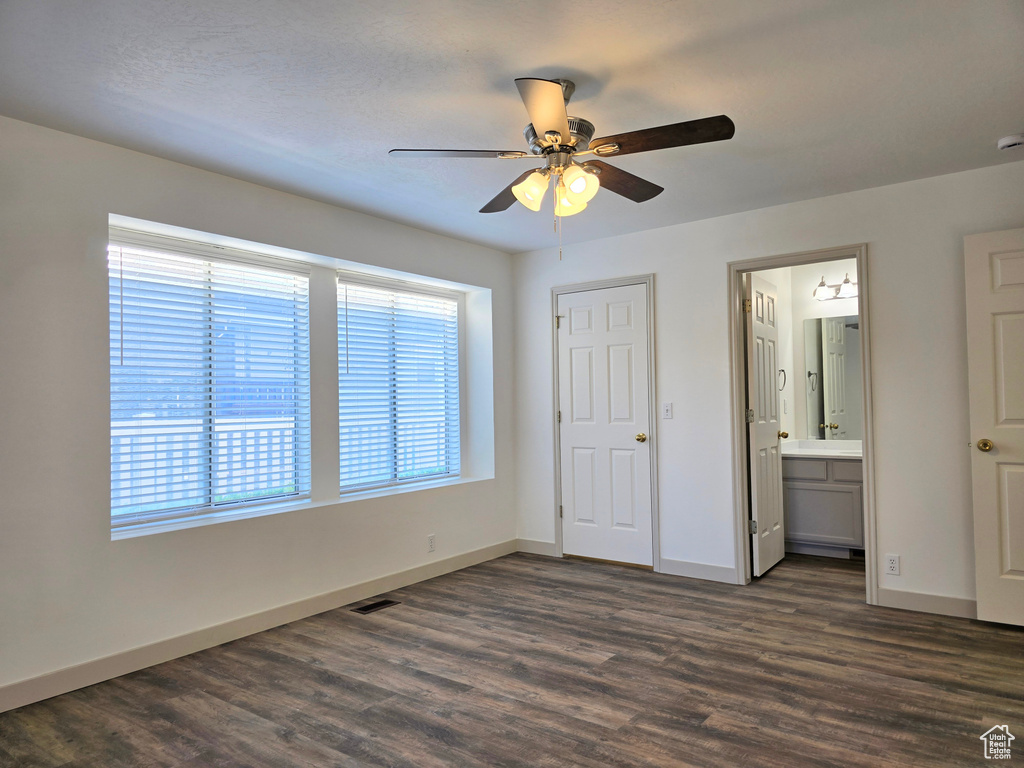 Unfurnished bedroom featuring dark wood-style flooring, baseboards, connected bathroom, and ceiling fan