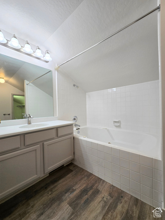 Bathroom with lofted ceiling, wood finished floors, vanity, and tiled shower / bath combo