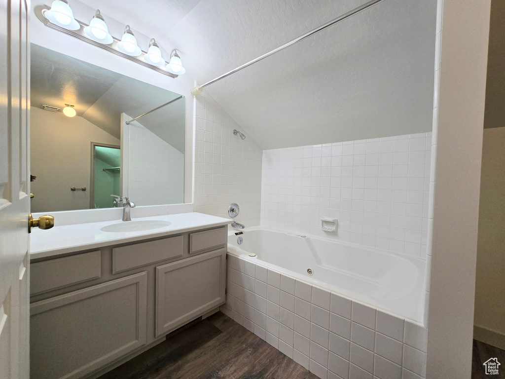 Full bath with wood finished floors, lofted ceiling, vanity, and a combined bath / shower with jetted tub