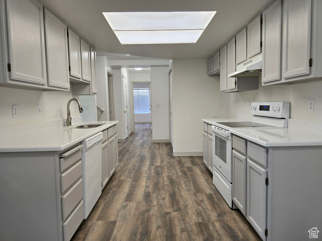 Kitchen featuring white appliances, gray cabinetry, under cabinet range hood, a sink, and dark wood finished floors