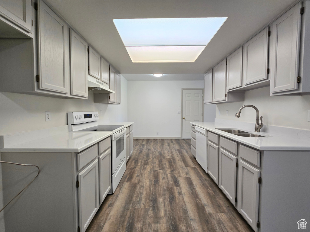 Kitchen with white appliances, gray cabinets, a sink, and dark wood-type flooring