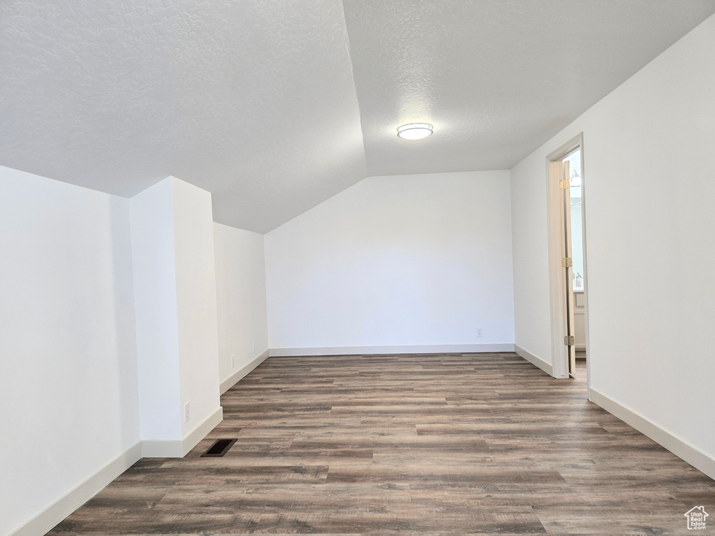 Bonus room featuring lofted ceiling, wood finished floors, a textured ceiling, and baseboards