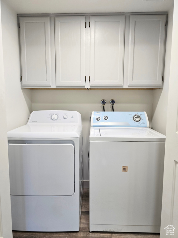 Washroom featuring washing machine and dryer, cabinet space, and wood finished floors