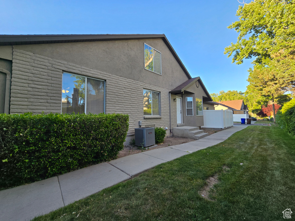 View of side of home featuring central AC unit, a lawn, and stucco siding