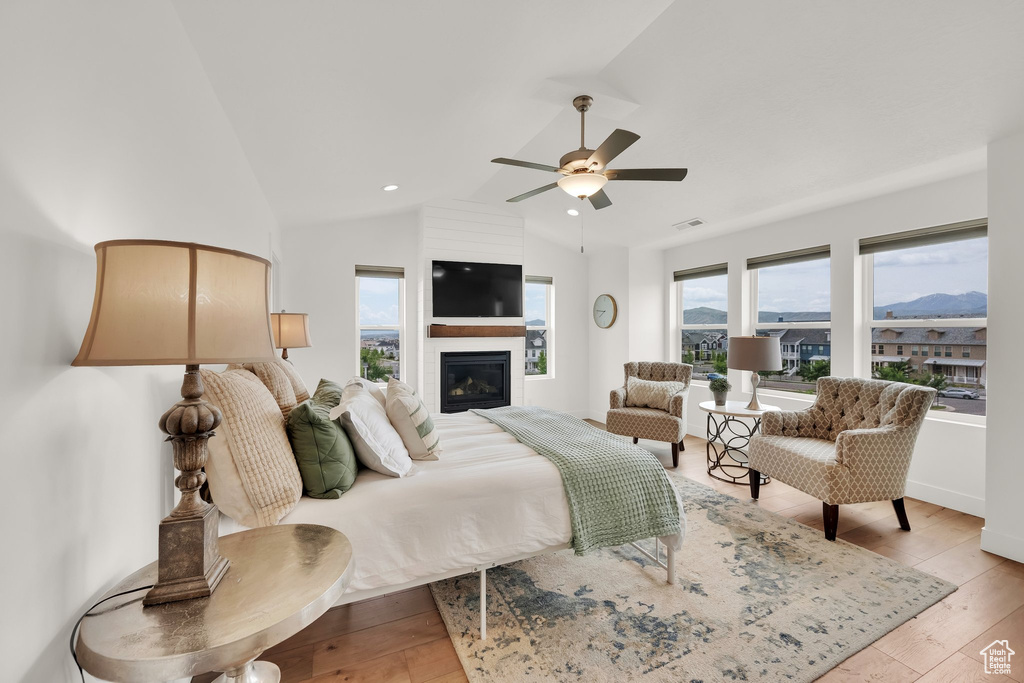 Bedroom featuring light wood-type flooring, lofted ceiling, a fireplace, and ceiling fan