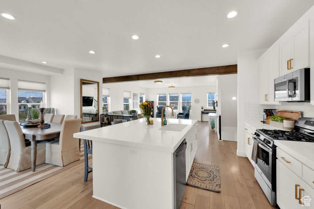 Kitchen with appliances with stainless steel finishes, open floor plan, a sink, light wood finished floors, and a kitchen island with sink