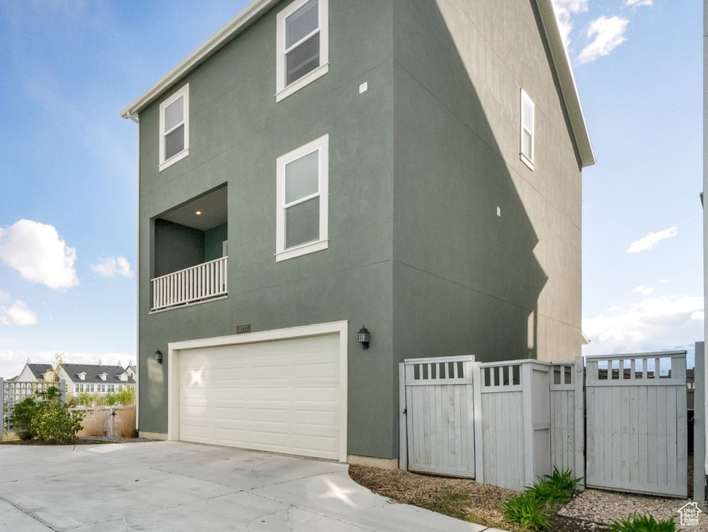 View of side of home featuring a gate, an attached garage, stucco siding, and driveway