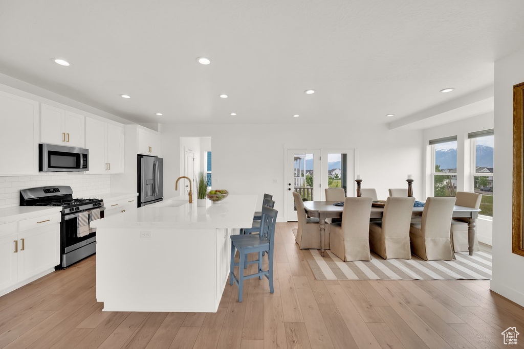 Kitchen featuring stainless steel appliances, a kitchen island with sink, light countertops, a sink, and white cabinets