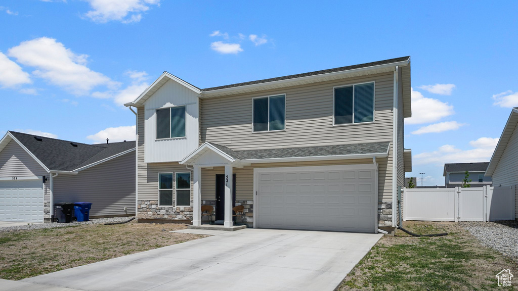View of front of property with stone siding, driveway, an attached garage, and a gate