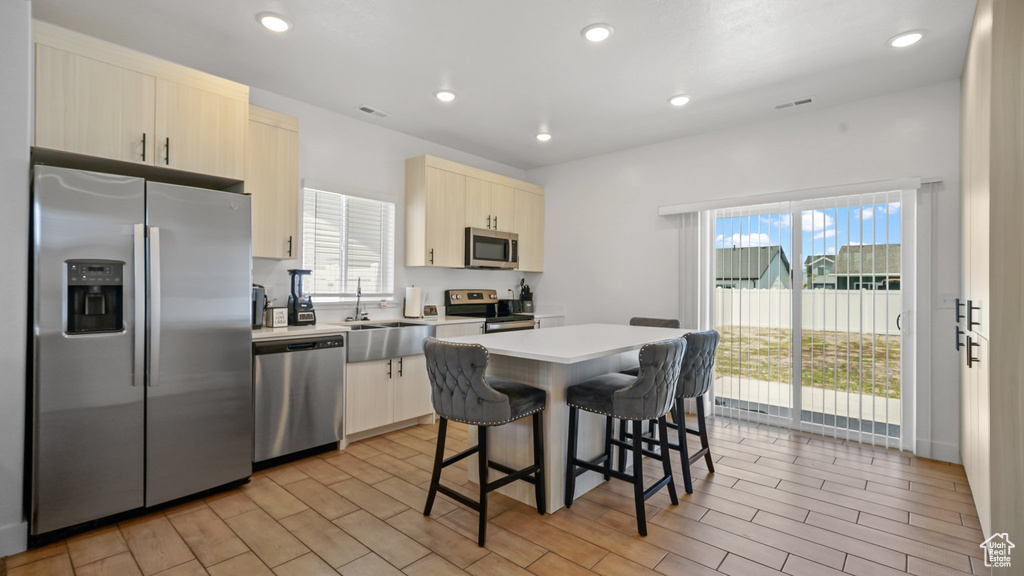 Kitchen with appliances with stainless steel finishes, a sink, a breakfast bar area, a center island, and light countertops