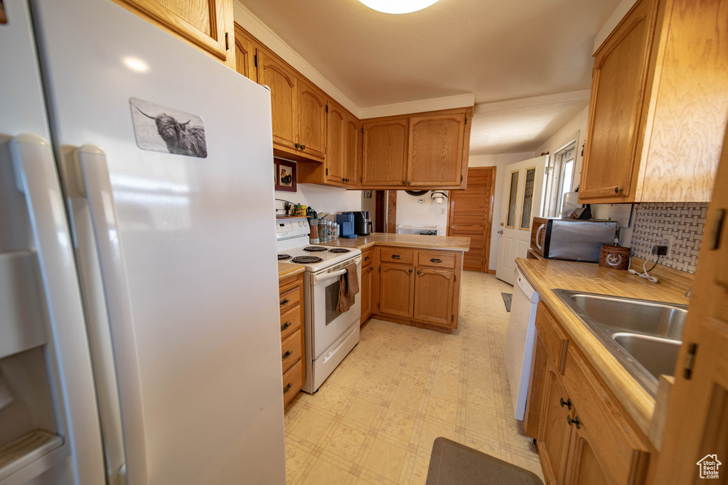 Kitchen featuring white appliances, a sink, light flooring, light countertops, and a peninsula