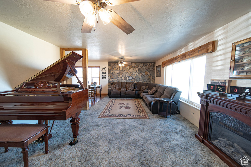 Carpeted living area with a ceiling fan, a fireplace, and a textured ceiling