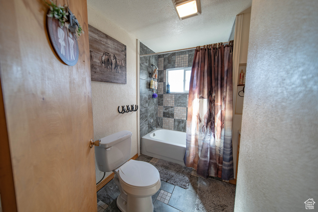 Bathroom featuring toilet, shower / tub combo, a textured ceiling, and a textured wall