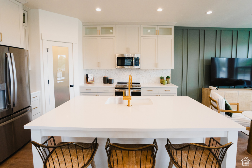 Kitchen with stainless steel appliances, decorative backsplash, light countertops, a sink, and a kitchen bar