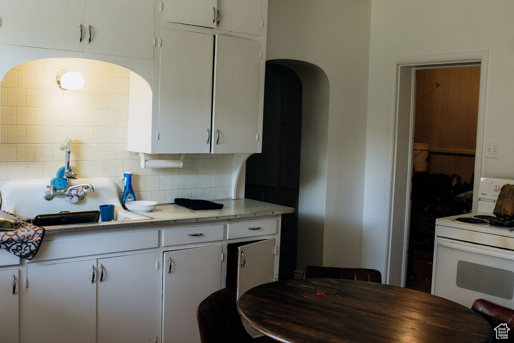 Kitchen with white range oven, decorative backsplash, light countertops, white cabinetry, and arched walkways