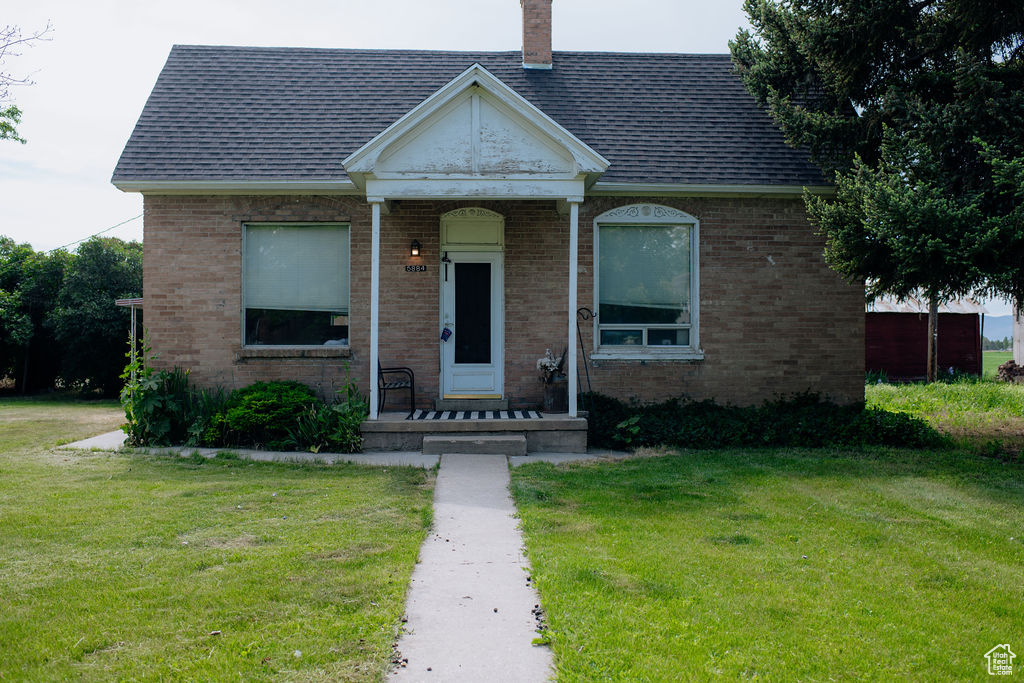 View of front of home with a front yard, brick siding, and a chimney