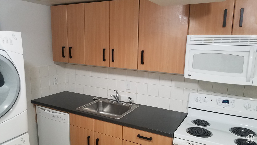 Kitchen with white appliances, washer / clothes dryer, a sink, dark countertops, and backsplash