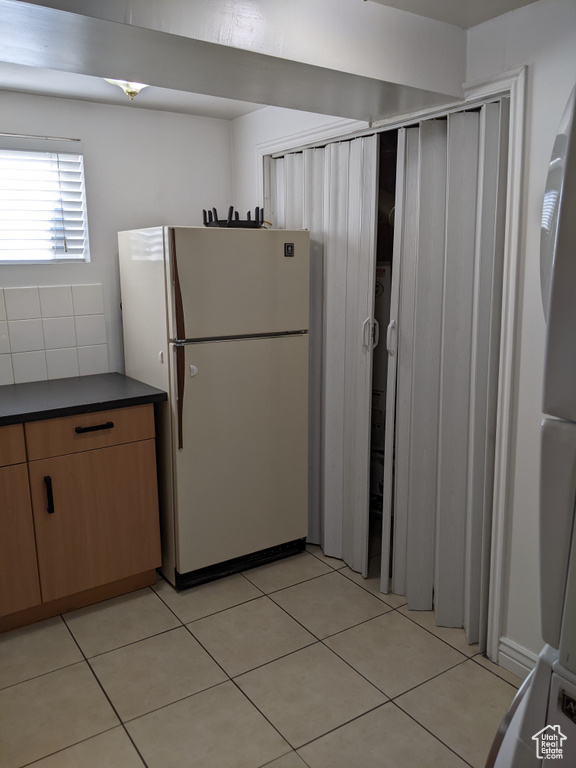 Kitchen with freestanding refrigerator, dark countertops, light tile patterned floors, and tasteful backsplash
