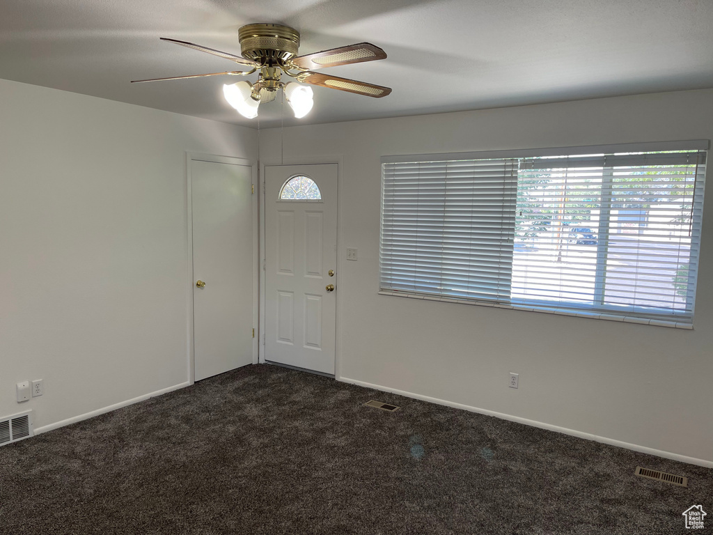 Foyer with dark colored carpet, ceiling fan, and baseboards