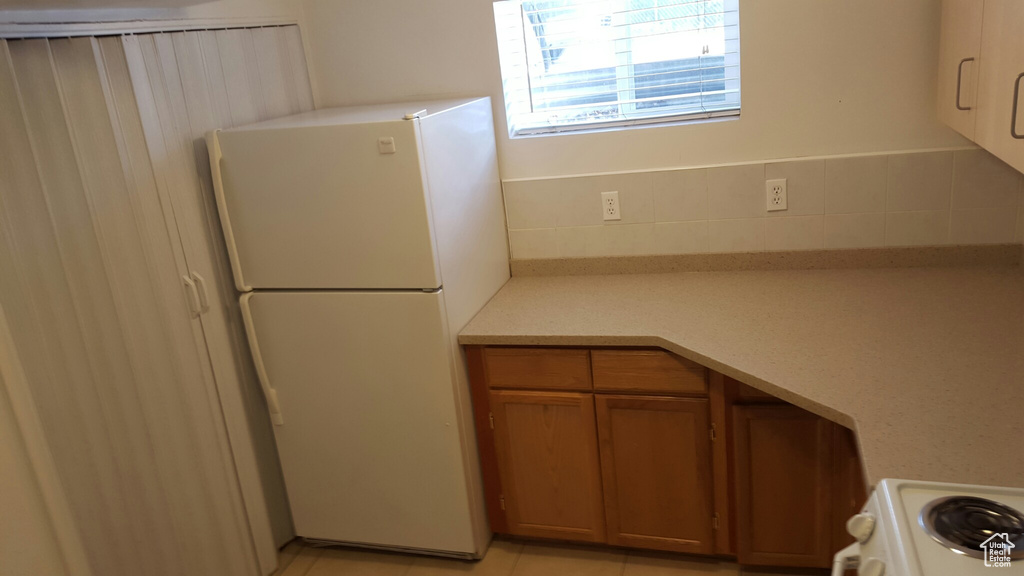 Kitchen featuring freestanding refrigerator, brown cabinetry, light countertops, and range