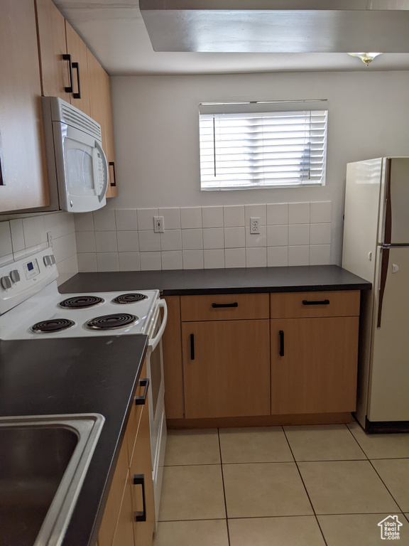 Kitchen featuring white appliances, dark countertops, tasteful backsplash, and a sink