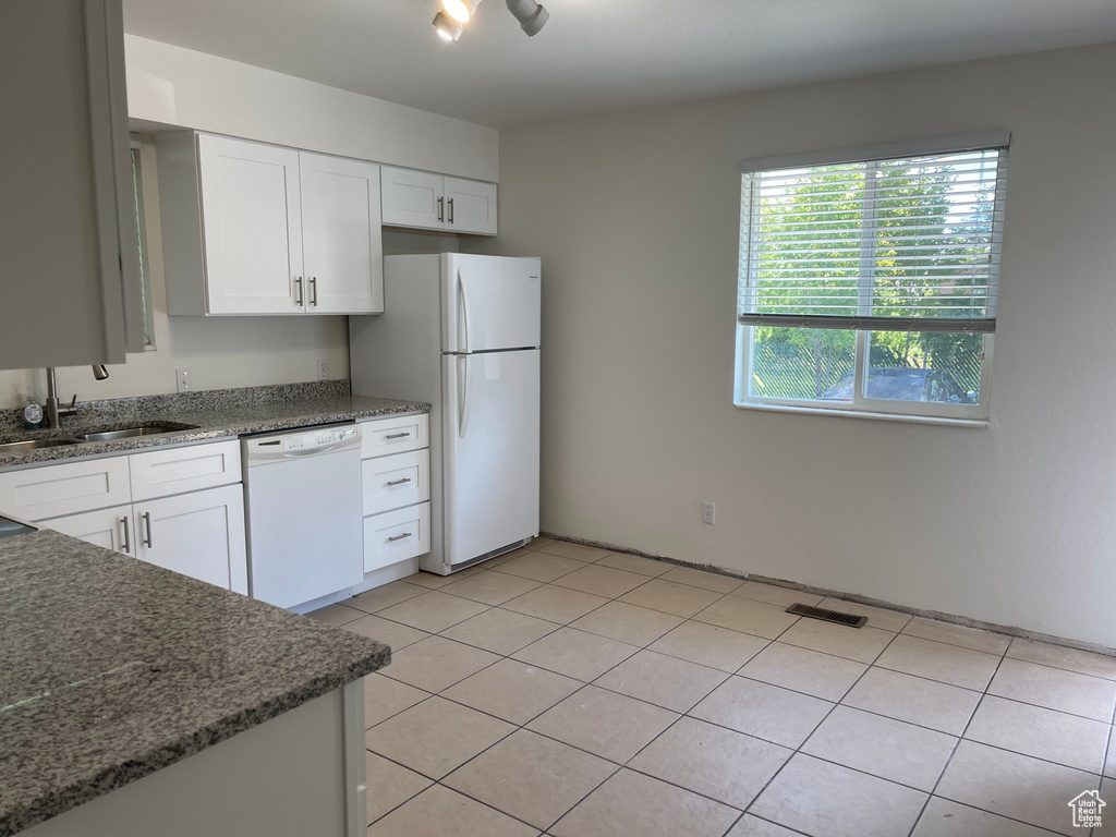 Kitchen featuring white appliances, a sink, white cabinetry, stone counters, and light tile patterned floors