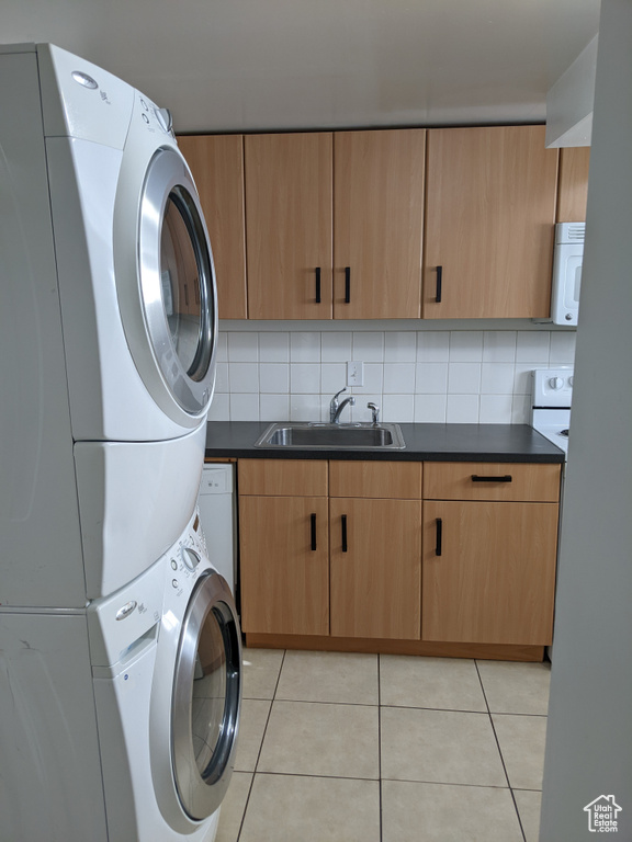 Laundry room featuring estacked washer and dryer, light tile patterned floors, and cabinet space
