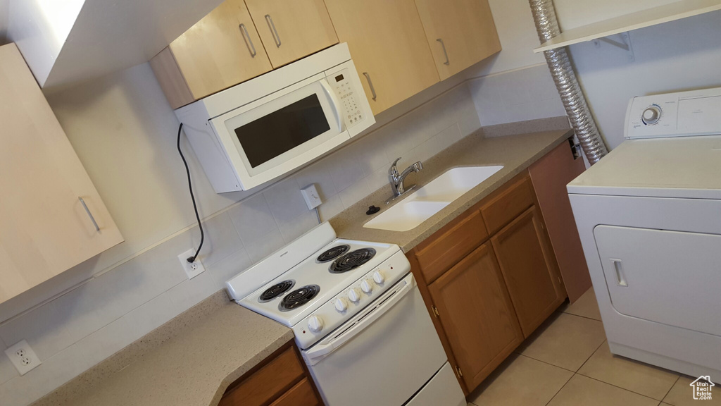 Kitchen with washer / dryer, white appliances, a sink, backsplash, and brown cabinetry