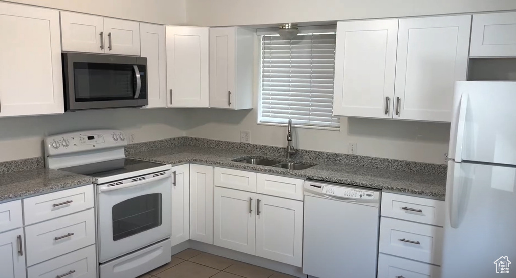 Kitchen with white appliances, a sink, white cabinetry, and stone counters
