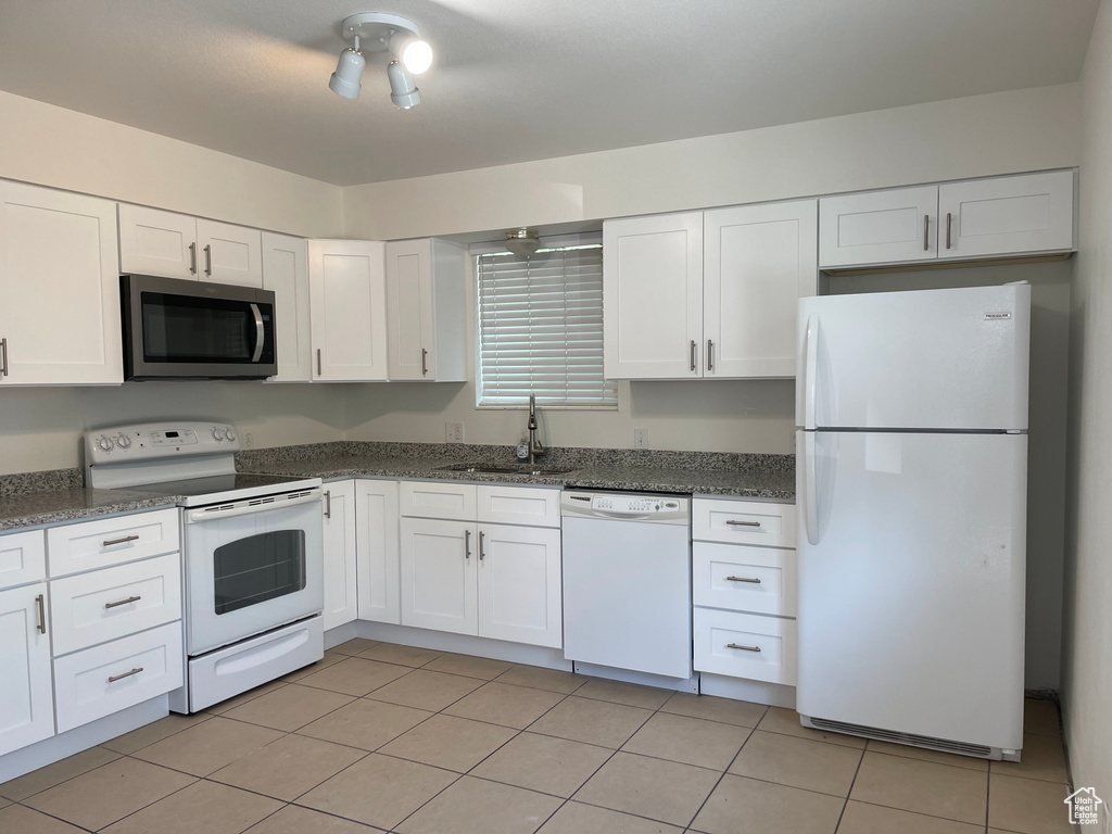 Kitchen featuring white appliances, a sink, white cabinetry, and dark stone counters